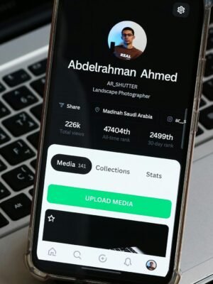 Close-up of a smartphone showing a photographer's profile on a laptop background.